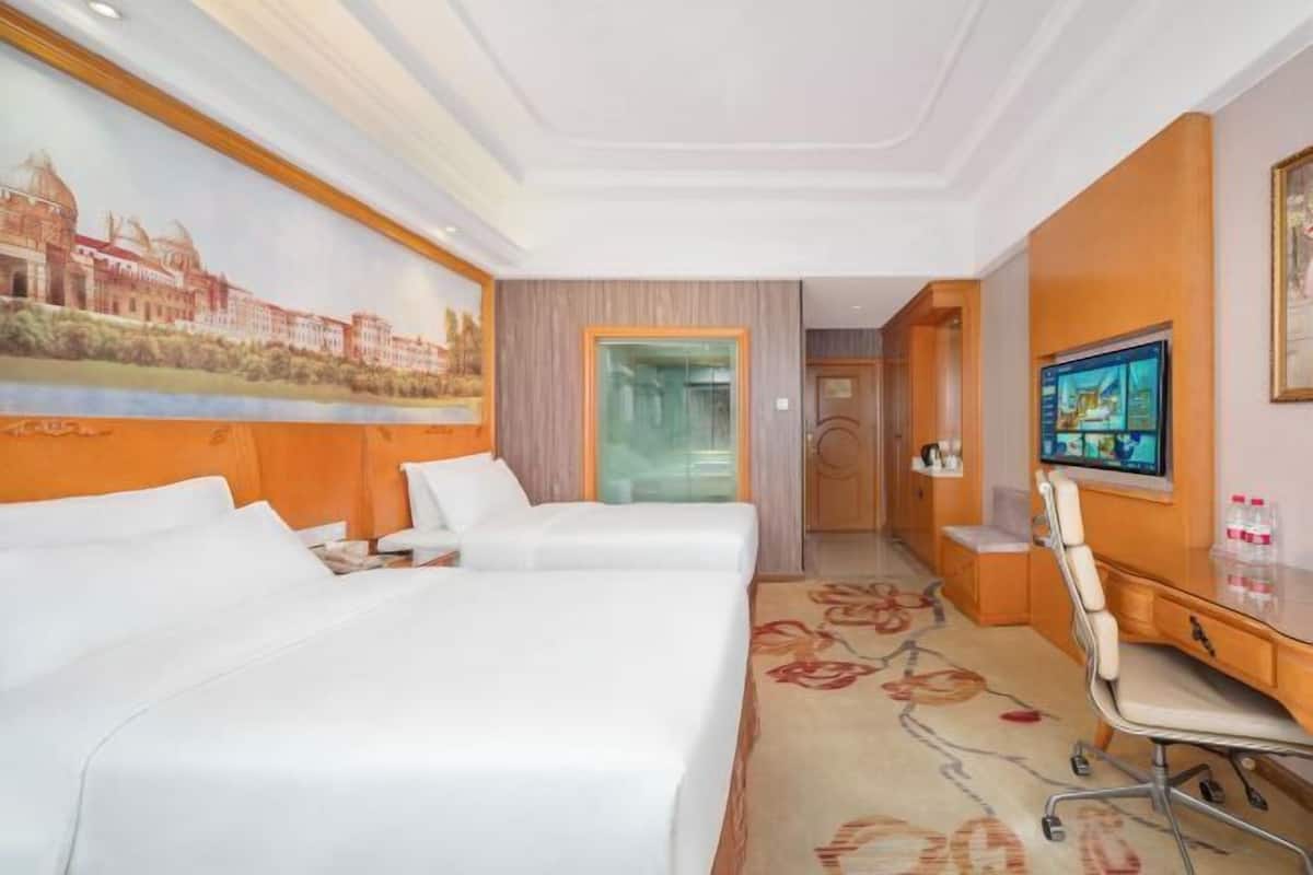 A hotel room with two beds, a desk, a chair, a television, and a mural on the wall.