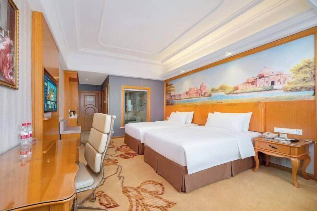 A hotel room with two beds, a desk, and a chair.