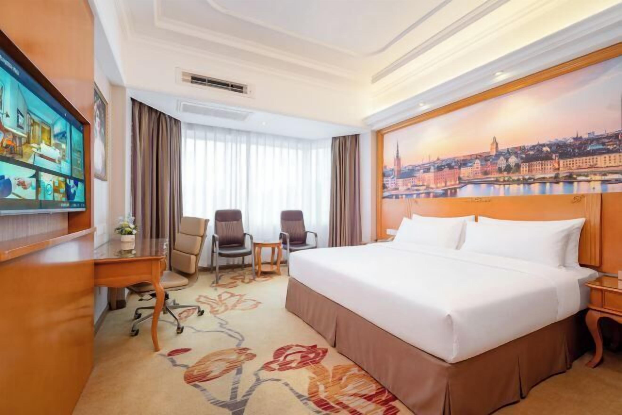 Habitación de hotel con una cama grande, un escritorio con silla, televisión y un cuadro de un paisaje urbano.