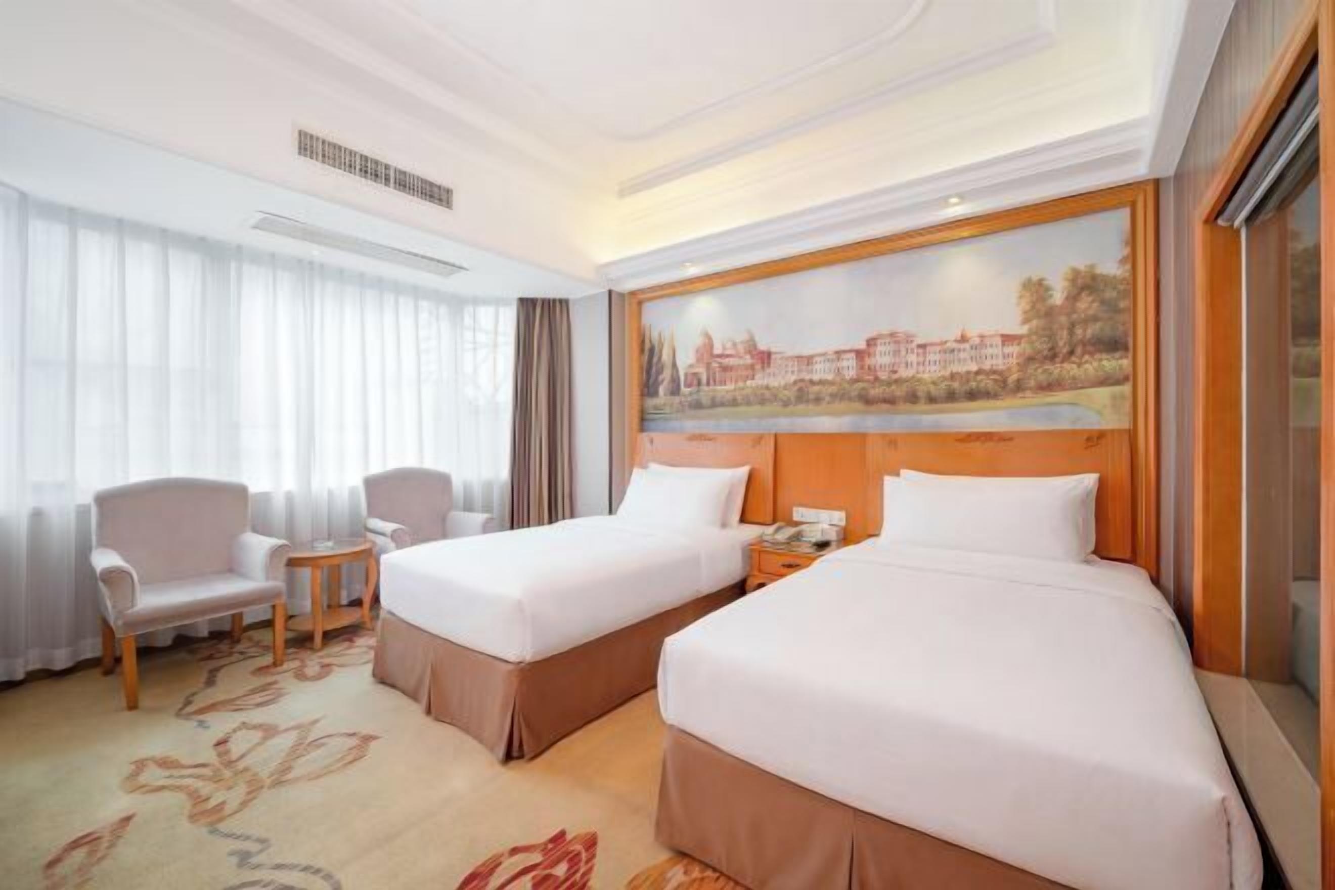 Ein Hotelzimmer mit zwei Betten, einem kleinen Tisch, einem Stuhl und einem Bild an der Wand.
