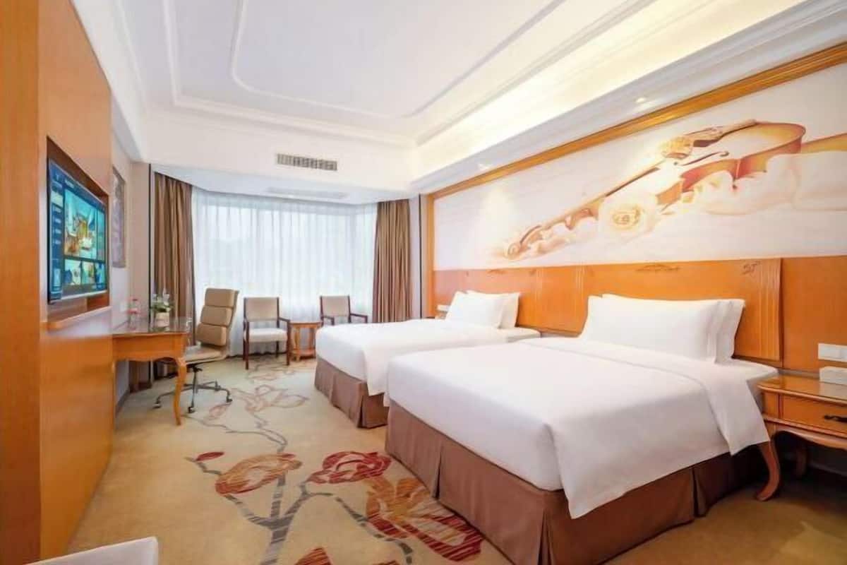A hotel room with two beds, a desk, a chair, and a television.