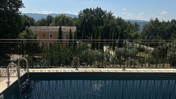 A swimming pool with a metal railing, surrounded by trees and a building in the background. - House with breathtaking views of the Luberon (Caseneuve)
