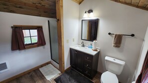 Ein Badezimmer mit Holzboden, einem Fenster mit Vorhängen, einem Waschbecken mit Spiegel, einem Handtuchhalter und einer Toilette.