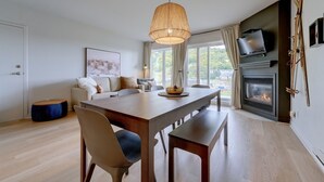 Una sala de estar moderna con una mesa de comedor de madera, un conjunto de sofás, una chimenea y un televisor montado en la pared.