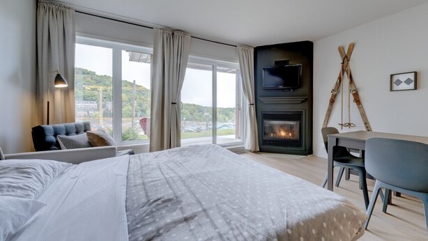 Una habitación de hotel moderna con una cama grande, chimenea, televisor y zona de comedor.