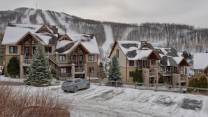 A row of multi-story buildings with a ski slope in the background. - L104-Condo ski in ski out /vélo in vélo out (Bromont)