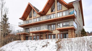 A multi-story building with a ski lodge design, featuring balconies and large windows. - L104-Condo ski in ski out /vélo in vélo out (Bromont)