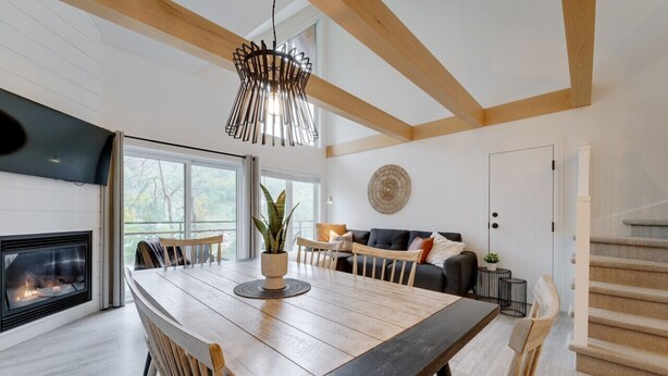A modern living room with a wooden dining table, a fireplace, and a large window.