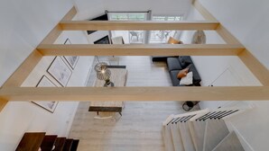 A spacious loft-style living area with a high ceiling, wooden beams, a sofa, and a dining table.