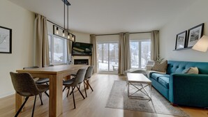 Un salon moderne comprenant un coin repas, un canapé et un téléviseur fixé au mur.