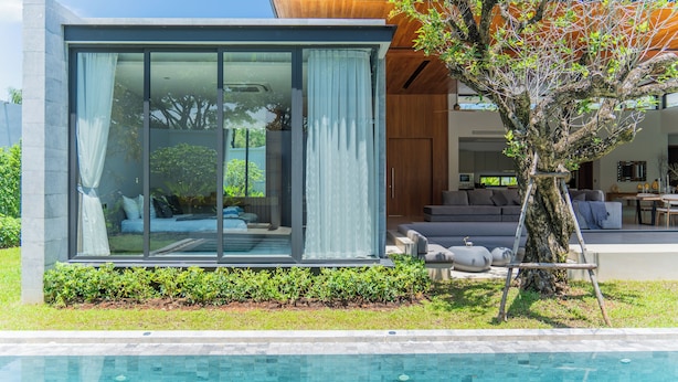 A modern house with a glass-enclosed room, a pool, and a tree.