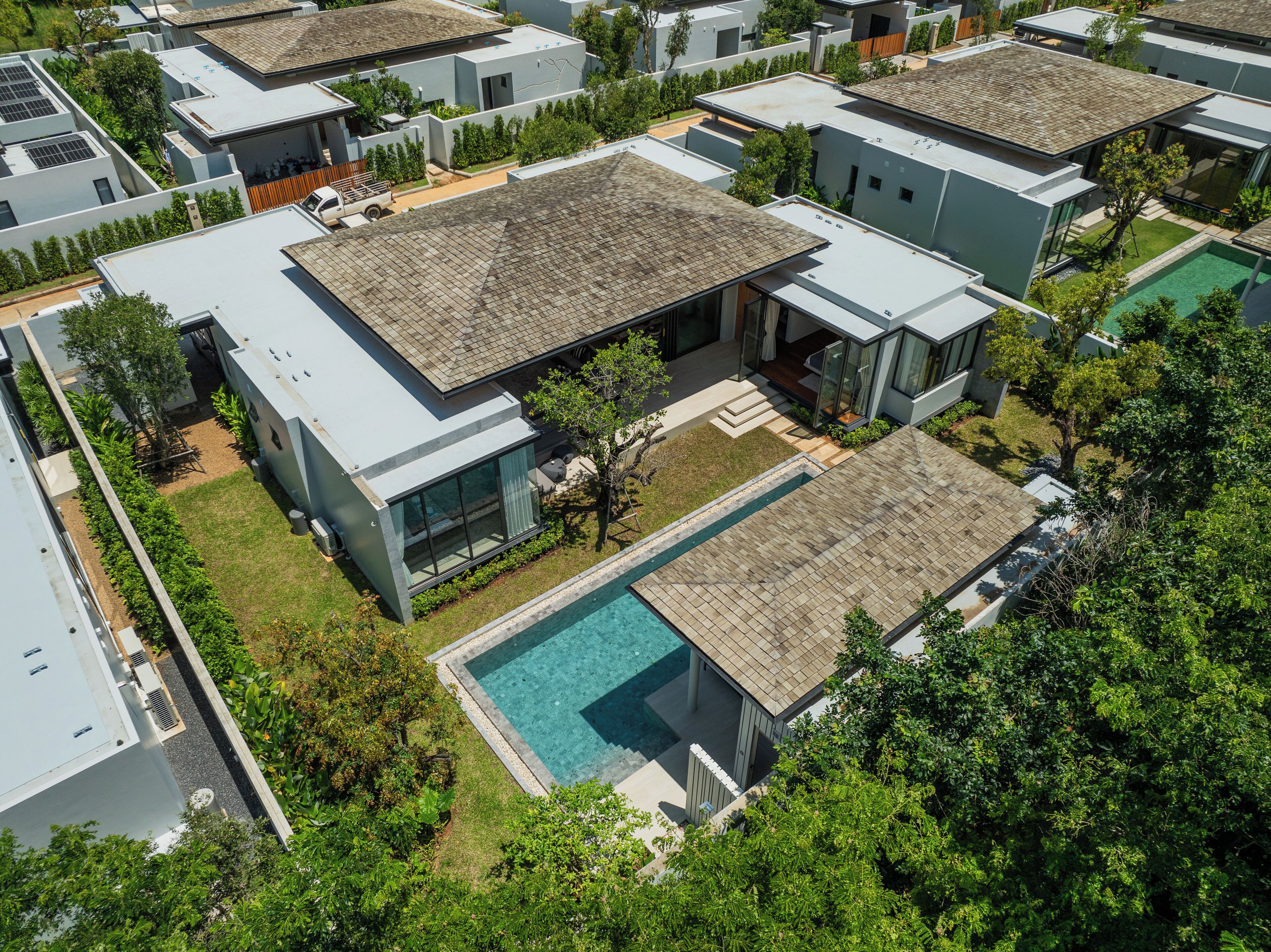 A modern residential complex with multiple detached houses, each featuring a swimming pool and surrounded by lush greenery.