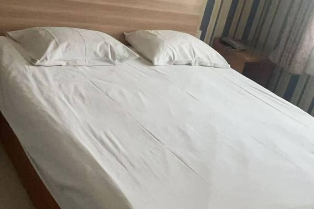 Una cama individual con ropa blanca, un cabecero de madera y cortinas a rayas al fondo.