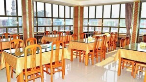 A dining area with multiple tables and chairs, large windows with city views, and a tiled floor. - huating hotel (Zhao County)