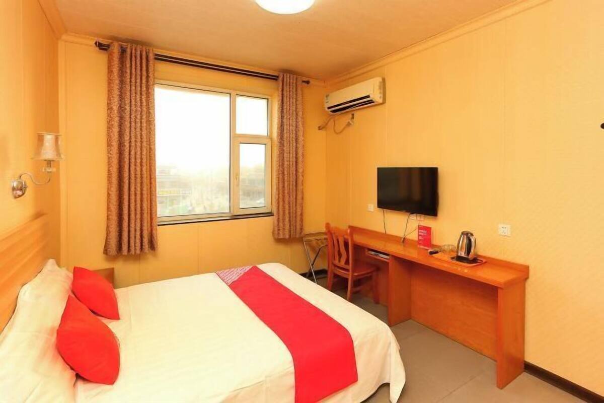 Habitación de hotel con cama, escritorio, silla, televisor y aire acondicionado.