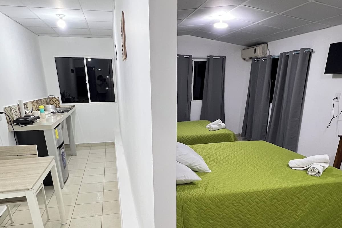 Habitación de hotel con dos camas, una mesita y un ventanal con cortinas.