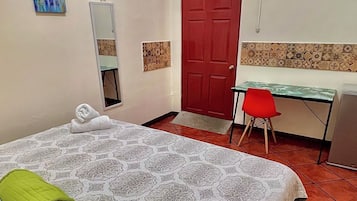 Una camera d'albergo con un letto, una scrivania, una porta rossa e un condizionatore d'aria.