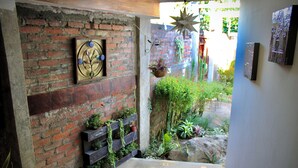 Una pared de ladrillo con un estante de madera que sostiene plantas, una decoración de estrella colgante y una obra de arte enmarcada.