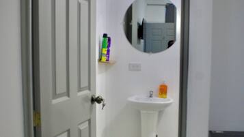Een badkamer met een witte deur, een witte wastafel, een spiegel en een plank met toiletartikelen.