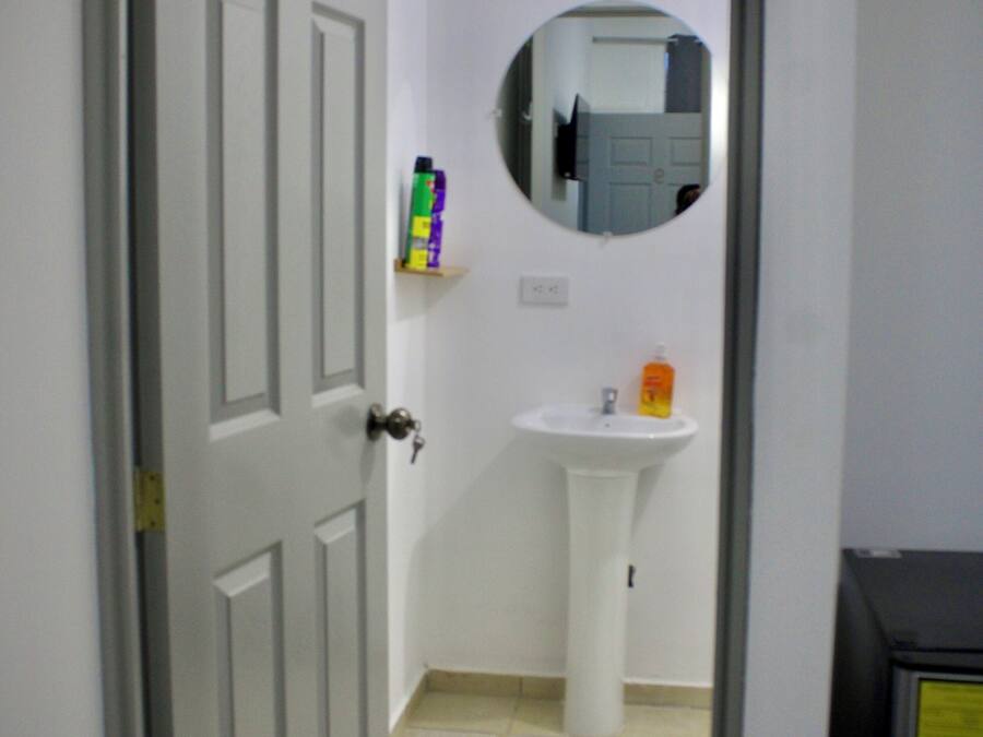 Een badkamer met een witte deur, een witte wastafel, een spiegel en een plank met toiletartikelen.