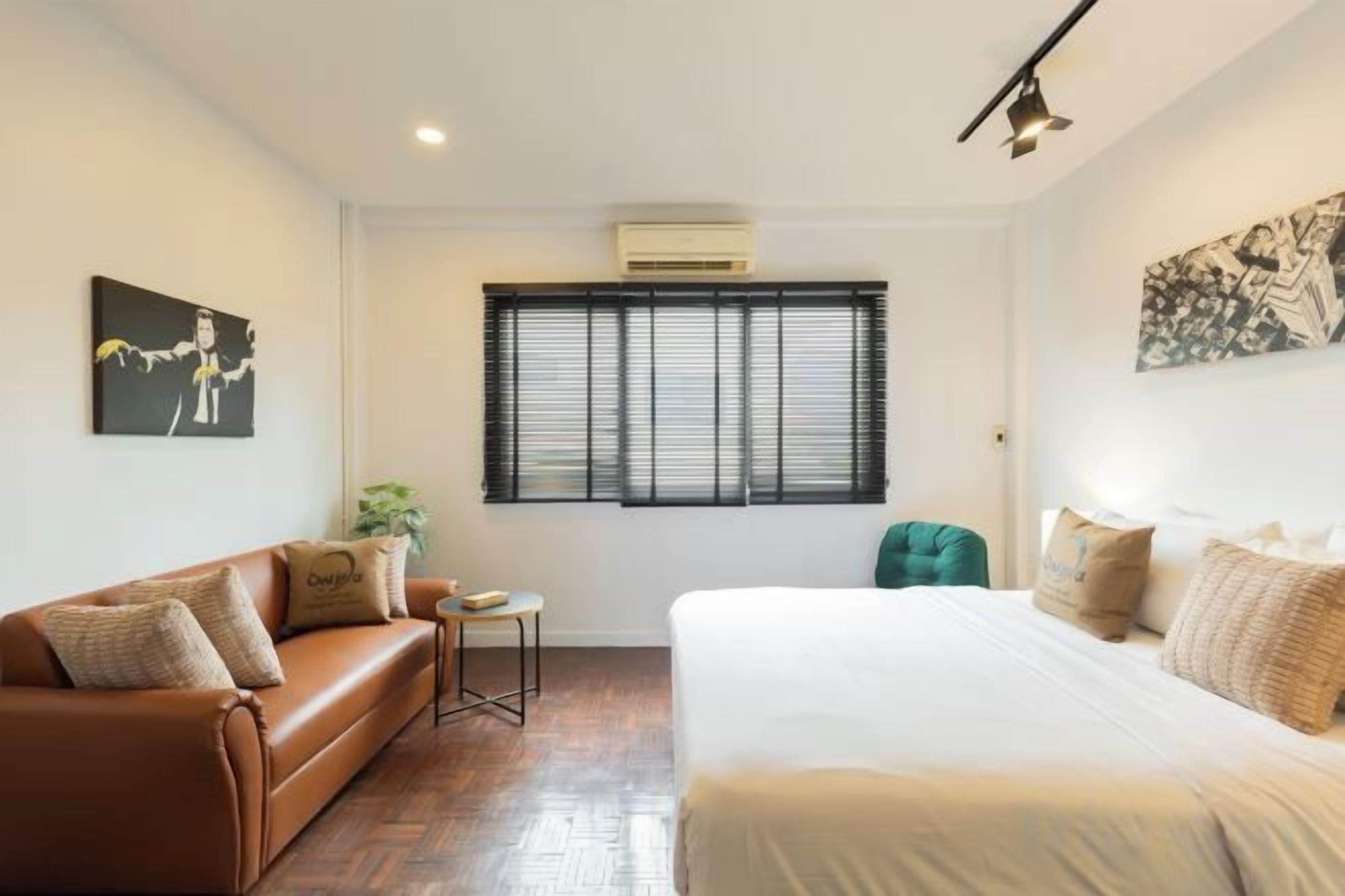 A hotel room with a bed, a sofa, a small table, and a window with blinds.