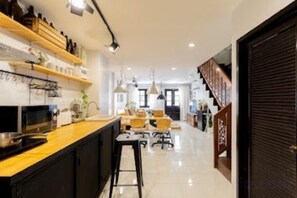 A modern kitchen with a central island, a dining area with chairs, and a staircase leading to another level. - Ombra House No26 (Chiang Mai)