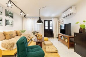 A living room with a sofa, a green armchair, a coffee table, a television, and a bookshelf. - Ombra House No26 (Chiang Mai)