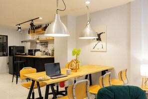 A modern kitchen with a dining area, featuring a wooden table, chairs, and pendant lighting. - Ombra House No26 (Chiang Mai)