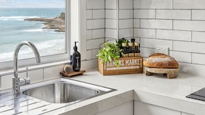 A kitchen with a stainless steel sink, a wooden crate with fresh produce, and a loaf of bread. - Boorolong 4 - Affordable Beachfront Escape with Convent Beach Views - Holiday Yamba (Yamba)