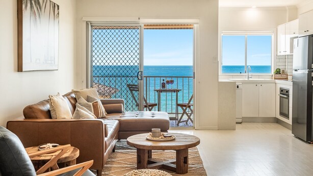 A living room with a sofa, a coffee table, and a view of the ocean through a balcony door. - Boorolong 4 - Affordable Beachfront Escape with Convent Beach Views - Holiday Yamba (Yamba)