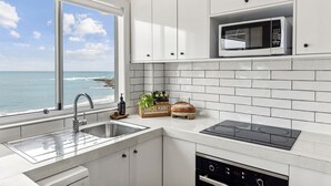 A modern kitchen with a view of the ocean, featuring a sink, stove, microwave, and white tiled backsplash. - Boorolong 4 - Affordable Beachfront Escape with Convent Beach Views - Holiday Yamba (Yamba)