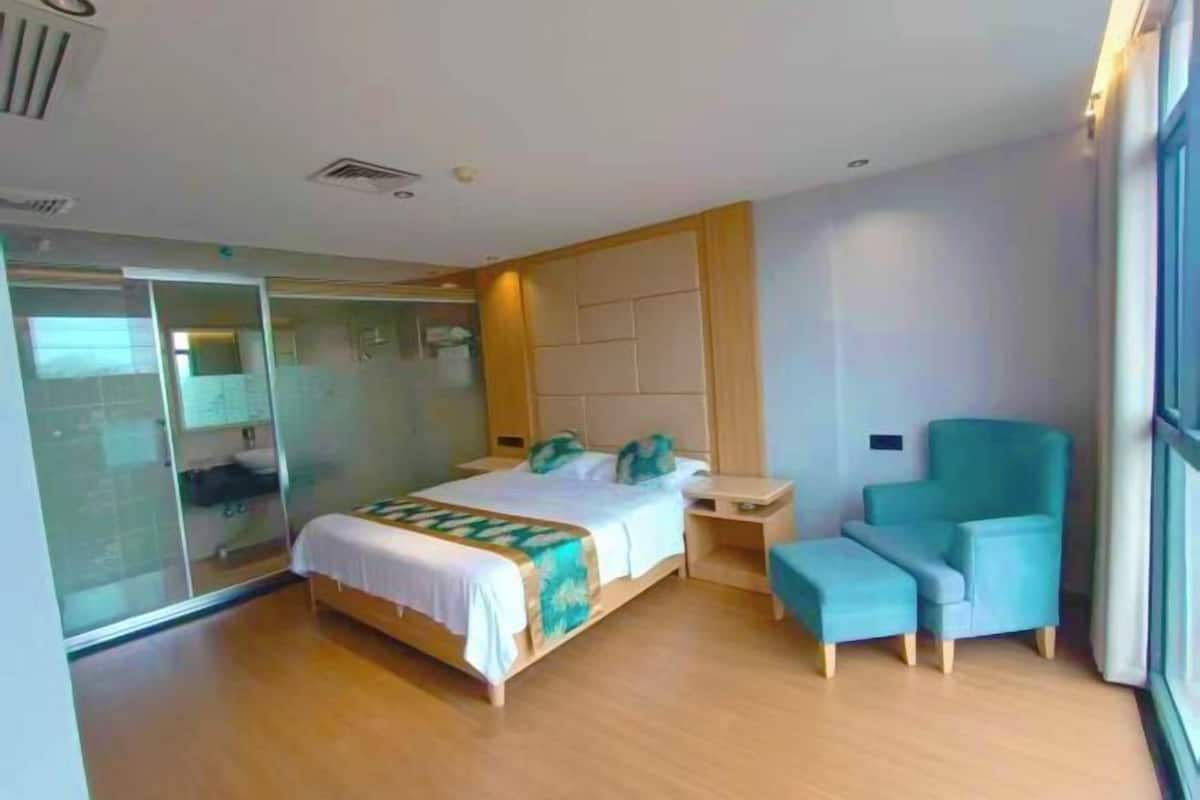 Quarto de hotel moderno com uma cama, área de estar com uma poltrona e divisória de vidro.