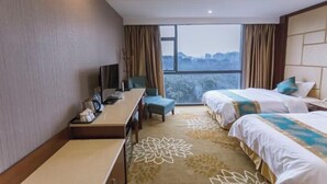Habitación de hotel con dos camas, un escritorio, una silla y un ventanal con vistas a la ciudad.