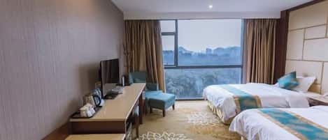 Een hotelkamer met twee bedden, een bureau, een stoel en een groot raam met uitzicht op de stadsgezicht.