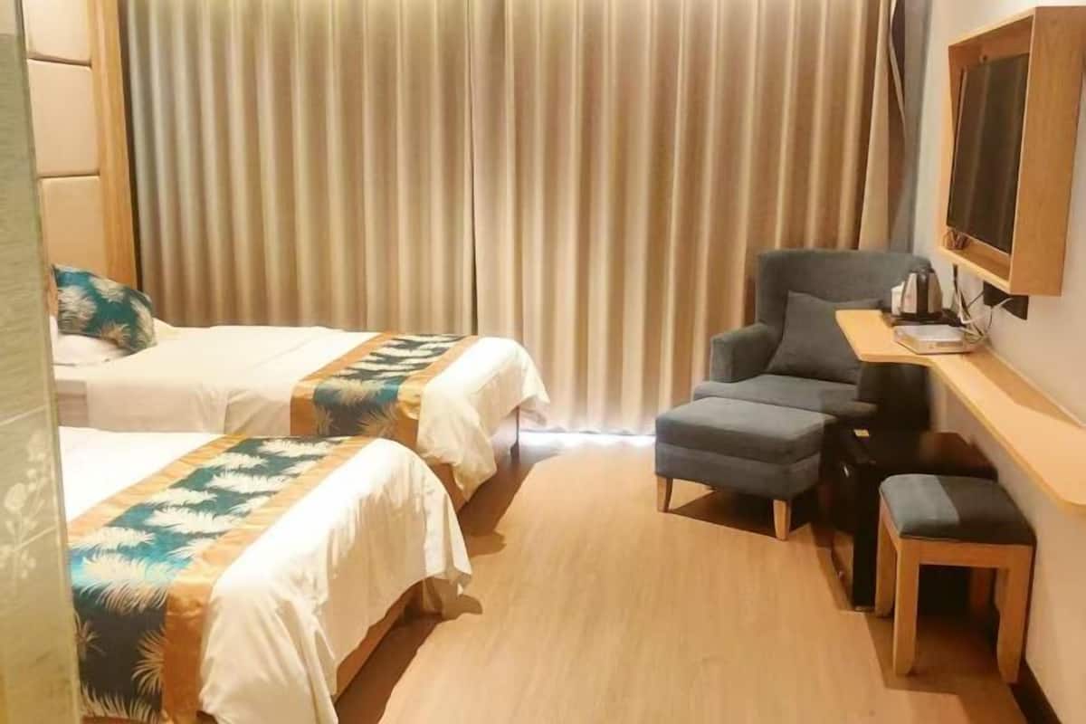 Quarto de hotel com duas camas, uma escrivaninha, uma cadeira e uma televisão.