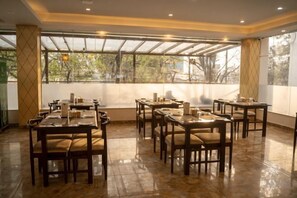 Ein Restaurant mit mehreren Tischen und Stühlen, großen Fenstern und Blick auf Bäume.