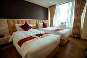 Ein Hotelzimmer mit zwei Betten, einem Kopfteil und einem mit Vorhängen versehenen Fenster.
