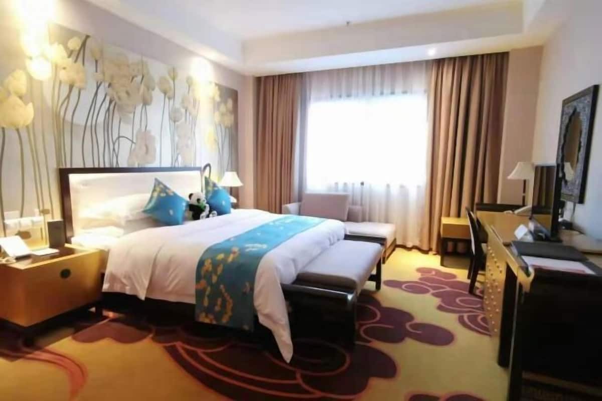 A hotel room with a bed, bedside table, lamp, and a large window with curtains.