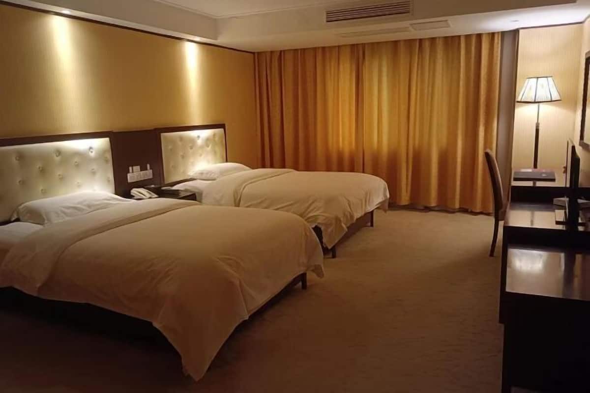 A hotel room with two beds, a desk, a chair, and a lamp.