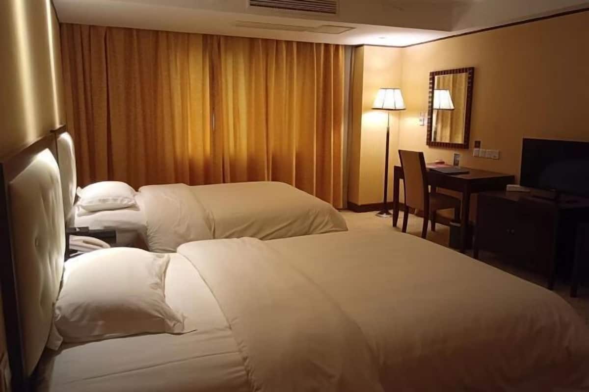 A hotel room with two beds, a desk, a chair, and a television.