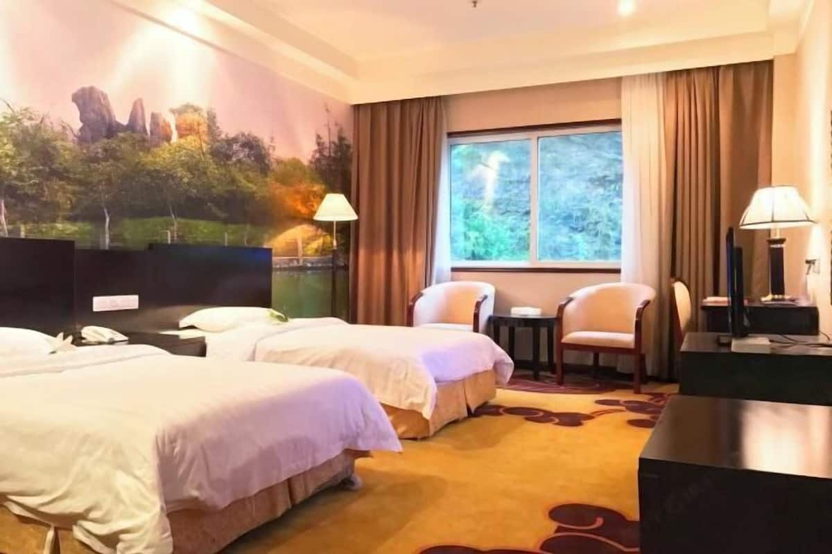 A hotel room with two beds, a large window with curtains, a small table, and a TV.