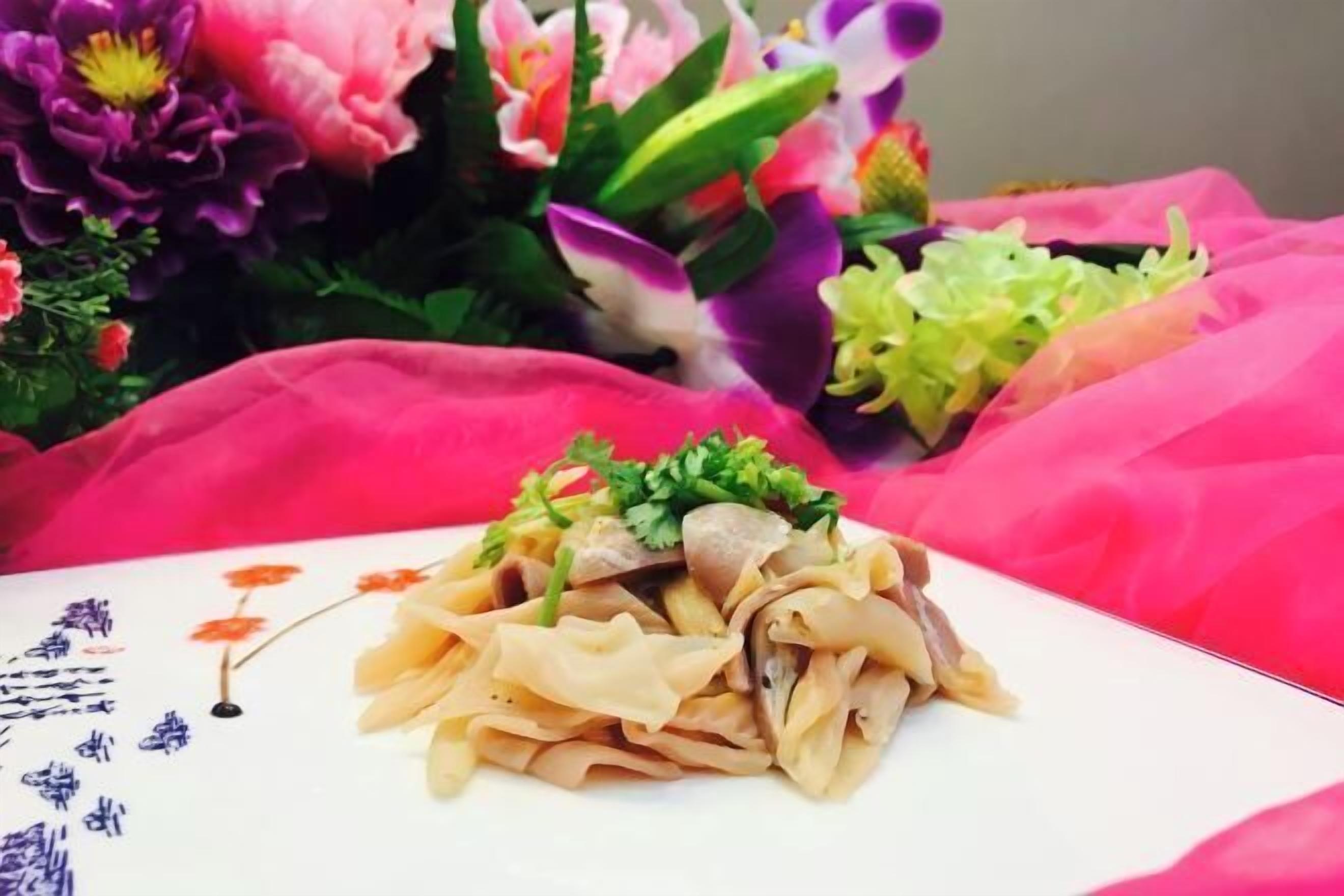 Un plato de fideos con una guarnición de hierbas verdes, sobre una mesa con diseño floral.