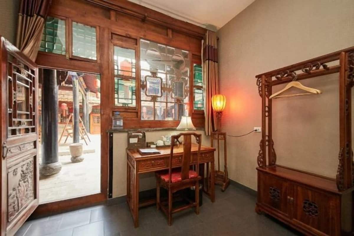 Ein Zimmer mit Holzschreibtisch, einem Stuhl, einem Kleiderhaken und einem großen Spiegel.