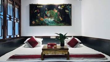 A hotel room with a bed, a decorative painting, a small table with a plant, and a window with curtains.