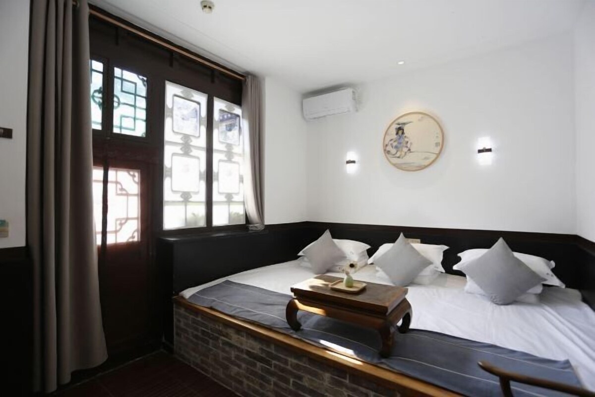 A room with a bed, a small table, a wall-mounted air conditioner, and a window with curtains.