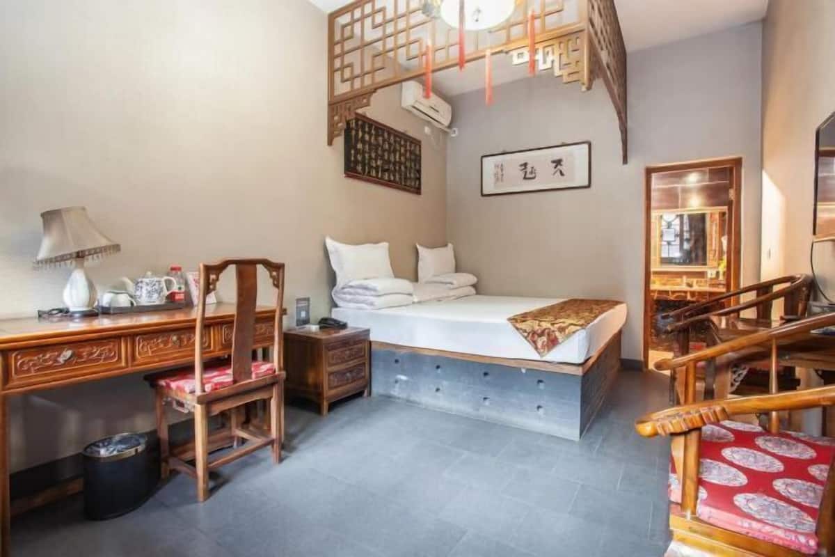 Ein traditionell eingerichteter Raum mit Bett, Schreibtisch, Stuhl und einem kleinen Tisch mit Lampe.