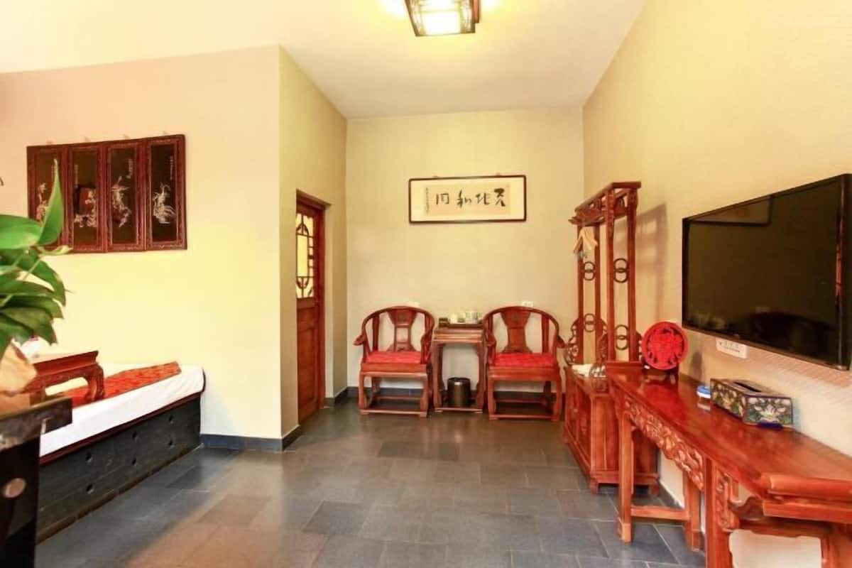 Ein traditionell eingerichtetes Zimmer mit einem Bett, Holzmöbeln, einem Fernseher und Kalligraphie an der Wand.