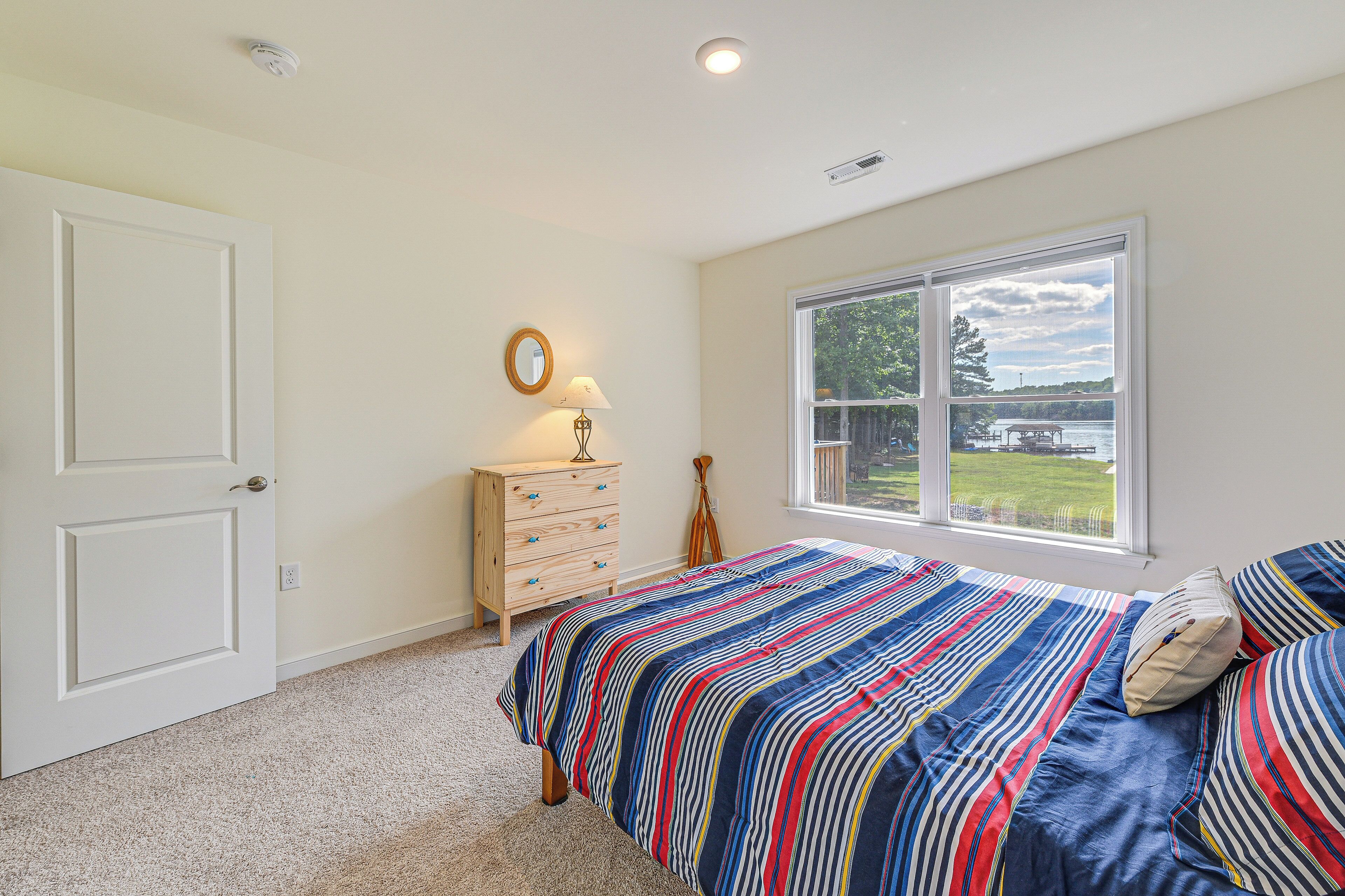 A bedroom with a bed, a dresser, a mirror, and a window with a view of a lake.