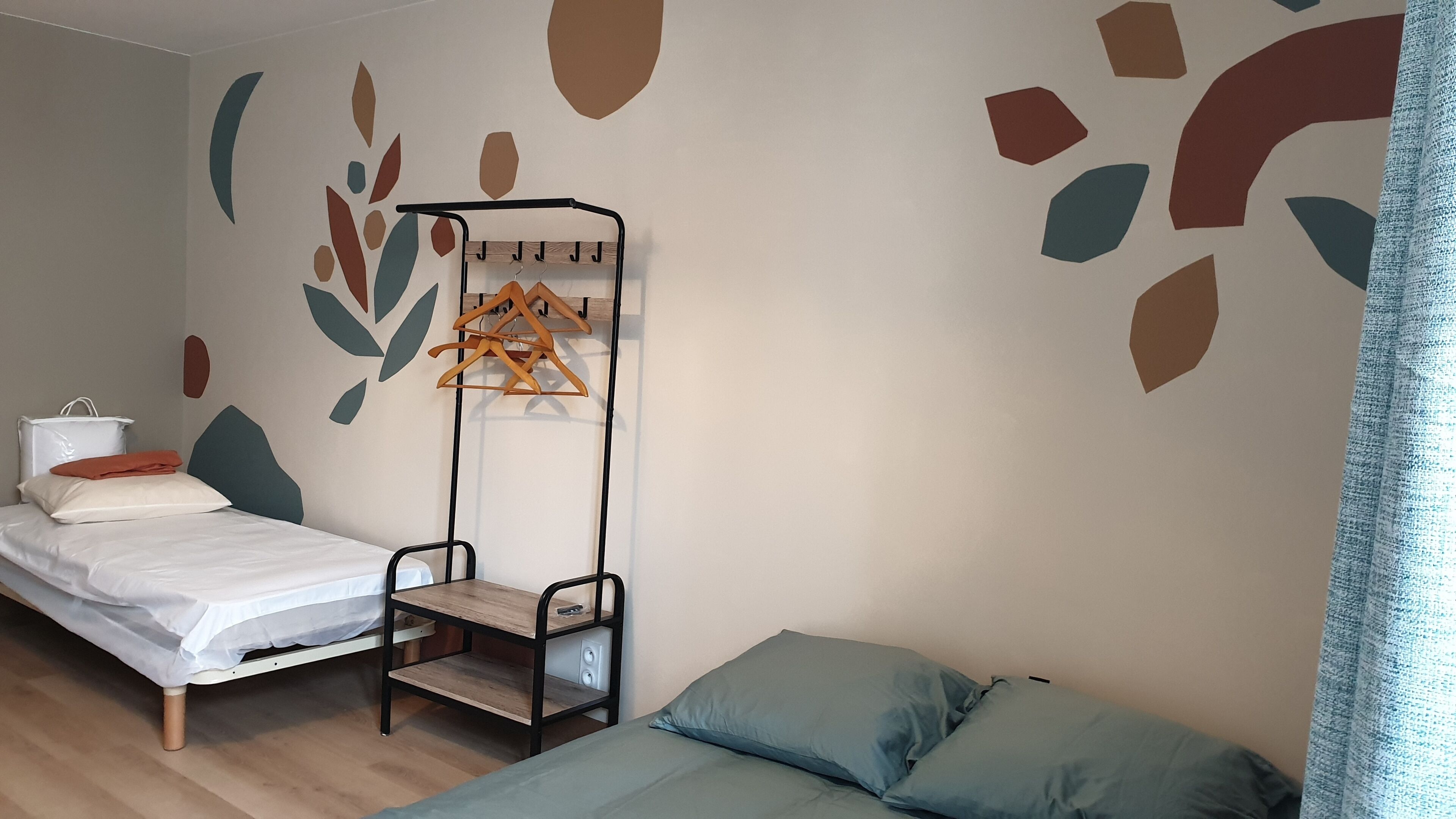 Una camera da letto con un letto, un comodino, un appendiabiti e una parete decorata con motivi a foglie astratte.