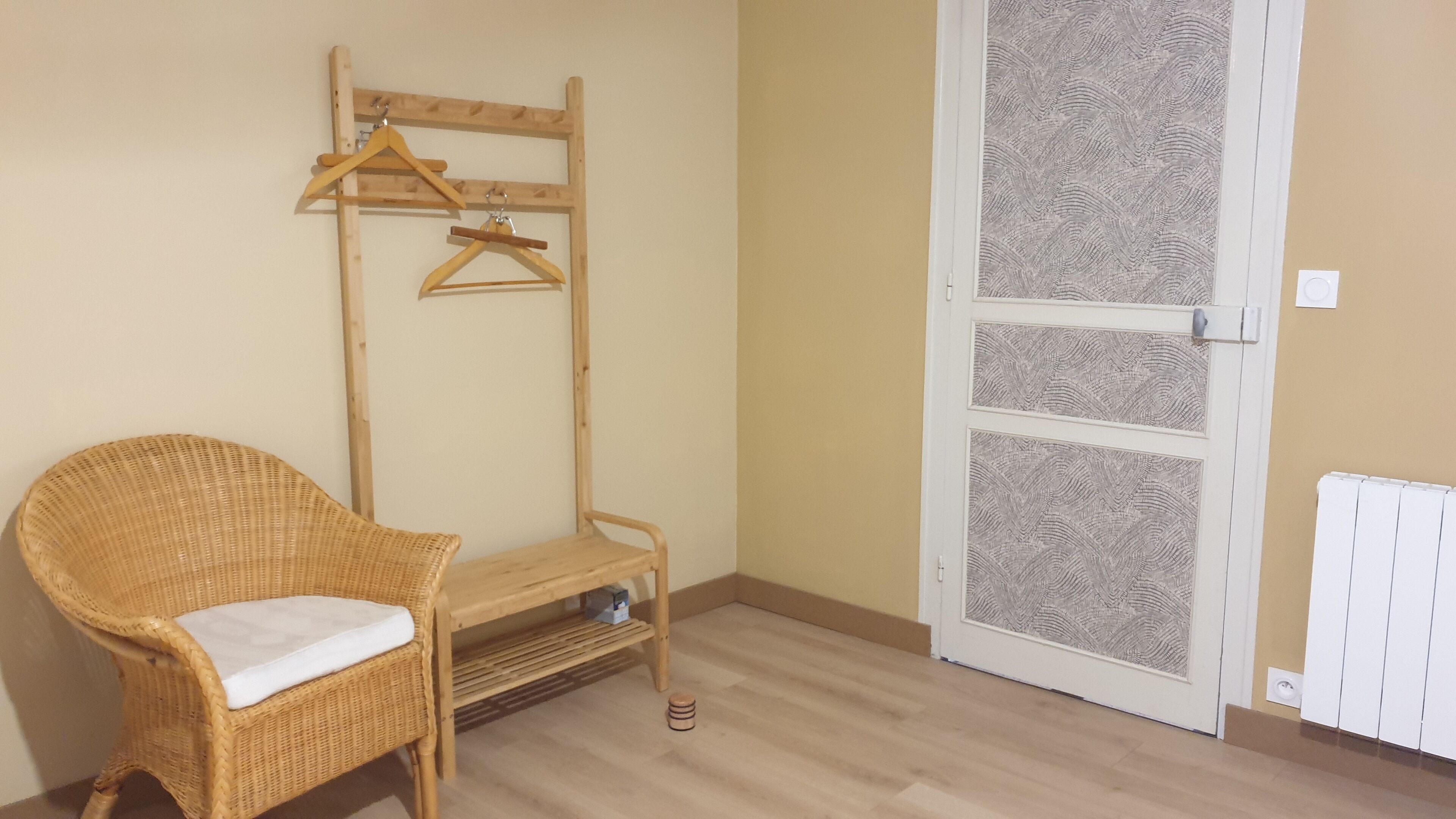 A room with a wicker chair, a wooden bench, a coat rack, and a patterned door.